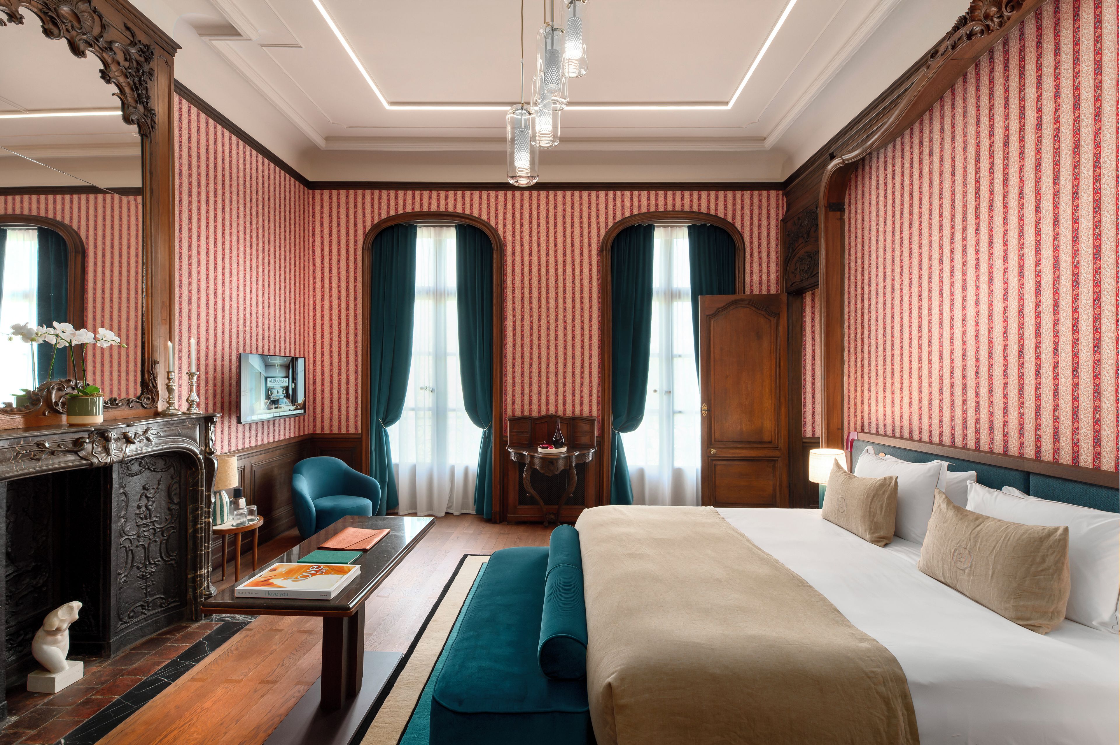 Habitación de hotel con una cama grande, un sofá, un escritorio con lámpara, una chimenea y vistas a la calle a través de una ventana.