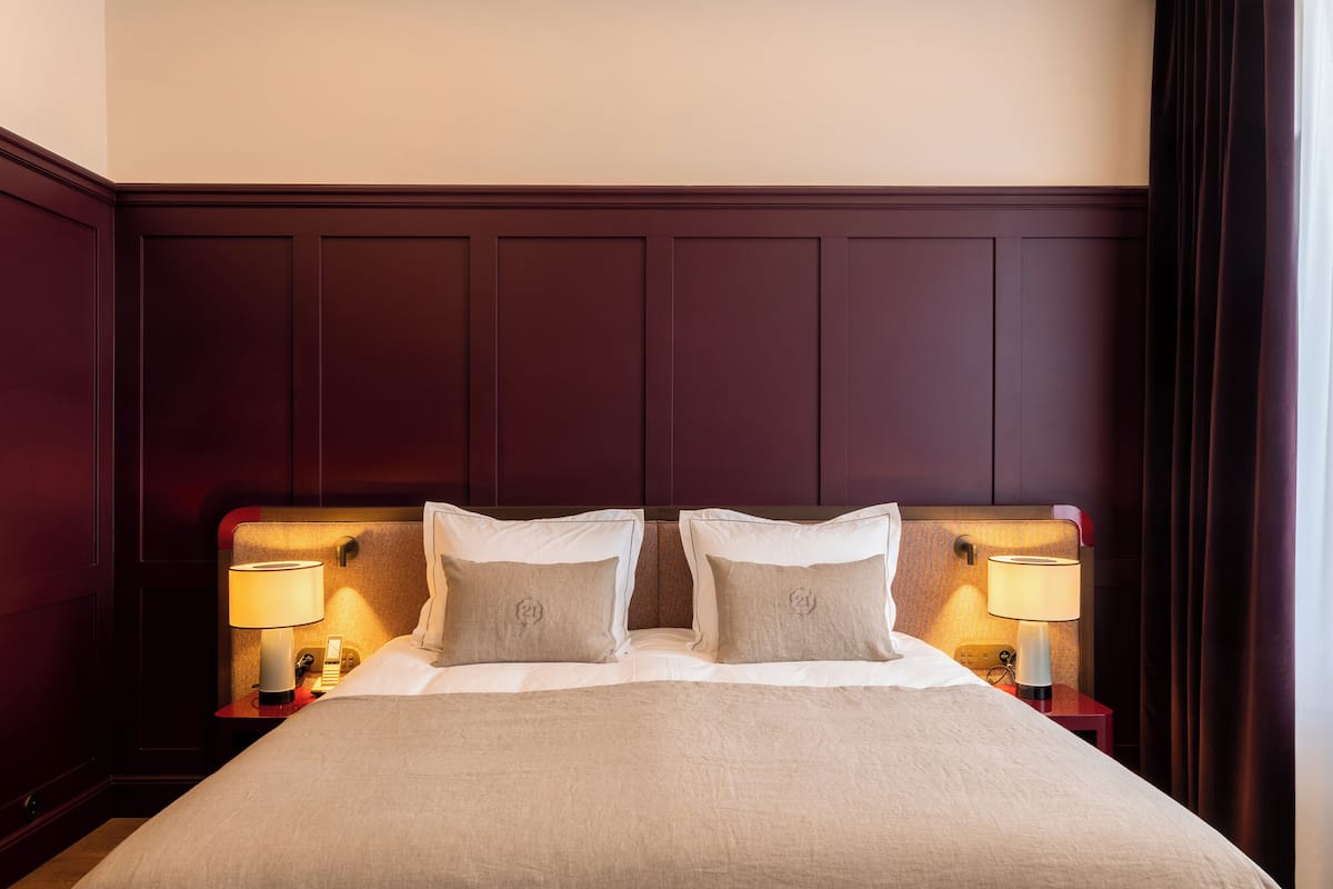A neatly made bed with a headboard, two bedside lamps, and a nightstand with a lamp.