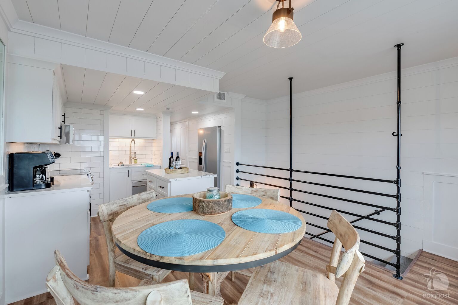 A modern kitchen with white cabinetry, a central island, and a dining area with a round wooden table and blue placemats.