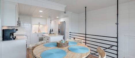 A modern kitchen with white cabinetry, a central island, and a dining area with a round wooden table and blue placemats.