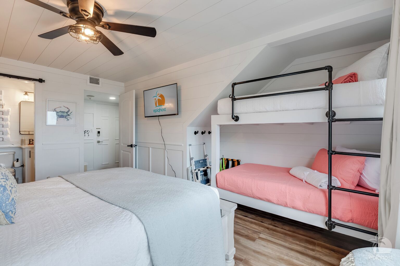 Ein Schlafzimmer mit einem Etagenbett, einem Deckenventilator, einem Bett mit einer weiß-blauen Musterdecke und einem kleinen Schreibtisch mit Stuhl.