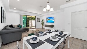 Uma sala de estar moderna com área de refeições, um sofá e uma TV fixada na parede.
