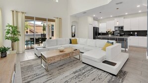 Ein großzügiger Wohnbereich mit einem weißen Sofa, einem Holztisch und Blick zur Küche.