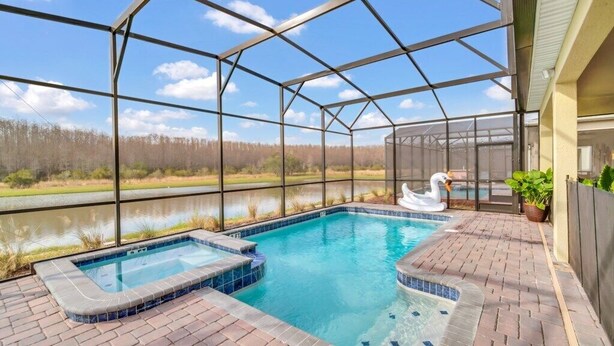 A covered outdoor swimming pool with a hot tub, surrounded by a brick patio, and overlooking a body of water. - Storey Lake 9 BR Villa With Games Room (Kissimmee)