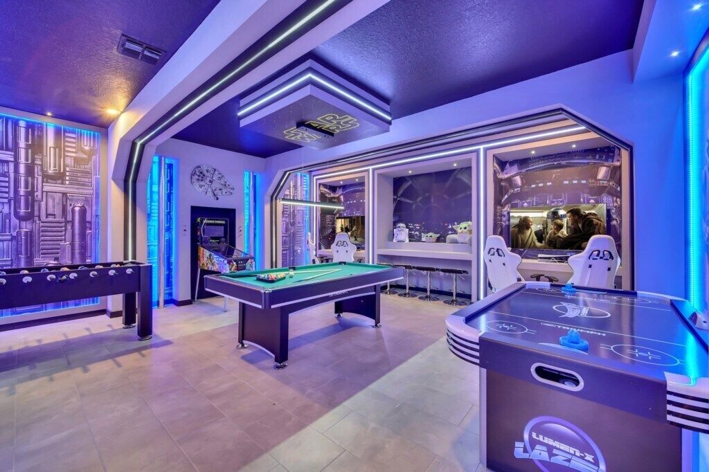 Una mesa de billar, una mesa de futbolín y una mesa de ping pong en una sala con diseño futurista, que incluye luces de neón y un ventanal grande.