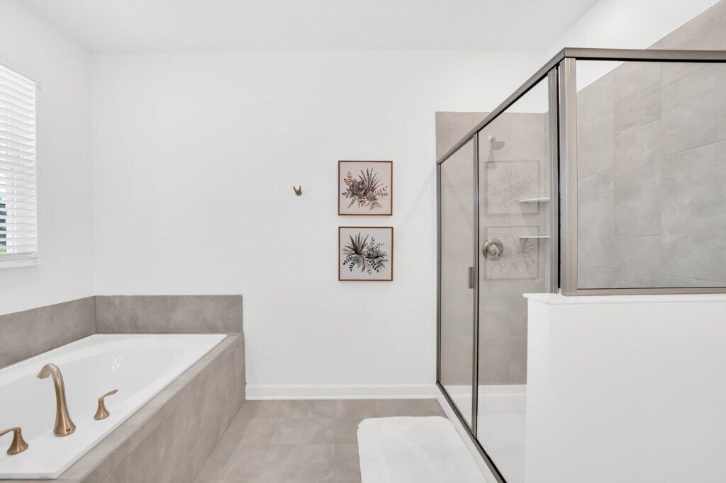 Een moderne badkamer met een bad, een glazen douchecabine en twee ingelijste botanische prints op de muur.