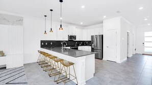 A modern kitchen with a central island, bar stools, stainless steel appliances, and pendant lighting. - Storey Lake 9 BR Villa With Games Room & Lake View (Kissimmee)
