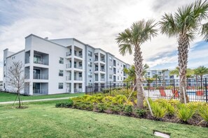 Un immeuble moderne à plusieurs étages, doté de balcons, entouré de pelouses bien entretenues et de palmiers.