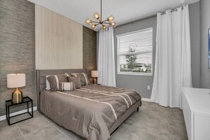 Une chambre moderne avec un grand lit, deux tables de chevet avec des lampes, un lustre et une fenêtre avec des stores.