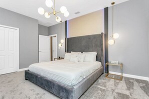 A modern bedroom with a large bed, a bedside table, and a nightstand. - Storey Lake 9 BR Villa With Games Room, Pool & Spa (Kissimmee)