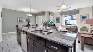 A modern kitchen with granite countertops, a double sink, and a dining area with a sofa and table.