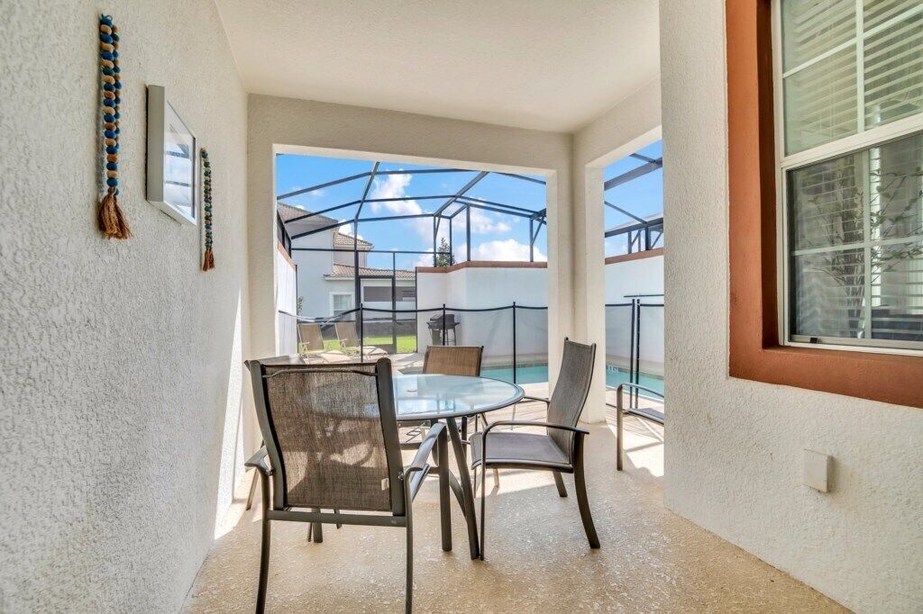 Un patio coperto con un tavolo e sedie in vetro, una piscina sullo sfondo e vista sulle case vicine.
