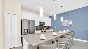 A modern kitchen with white cabinets, a central island with stools, a refrigerator, and a microwave.