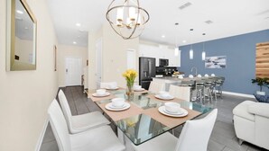 A modern dining area with a glass table, white chairs, and a central light fixture.