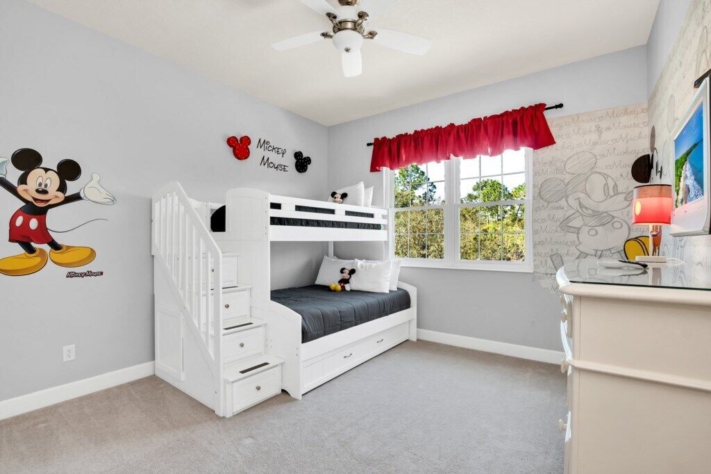 A child's bedroom with a bunk bed, Mickey Mouse wall decal, and a window with a red valance.