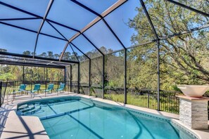 A covered outdoor swimming pool with a metal roof, surrounded by a fence, and a stone structure with a large bowl.