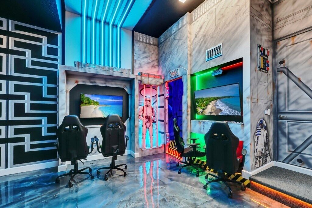 Une salle de jeux équipée de plusieurs fauteuils de jeu, d’un grand téléviseur et d’un mur décoré sur le thème de Star Wars.