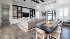 Un salón amplio con un sofá modular grande, un televisor de pantalla plana y un comedor con una mesa larga y sillas.