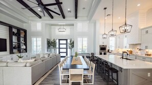 Una cocina amplia con una isla central, armarios blancos e iluminación colgante.