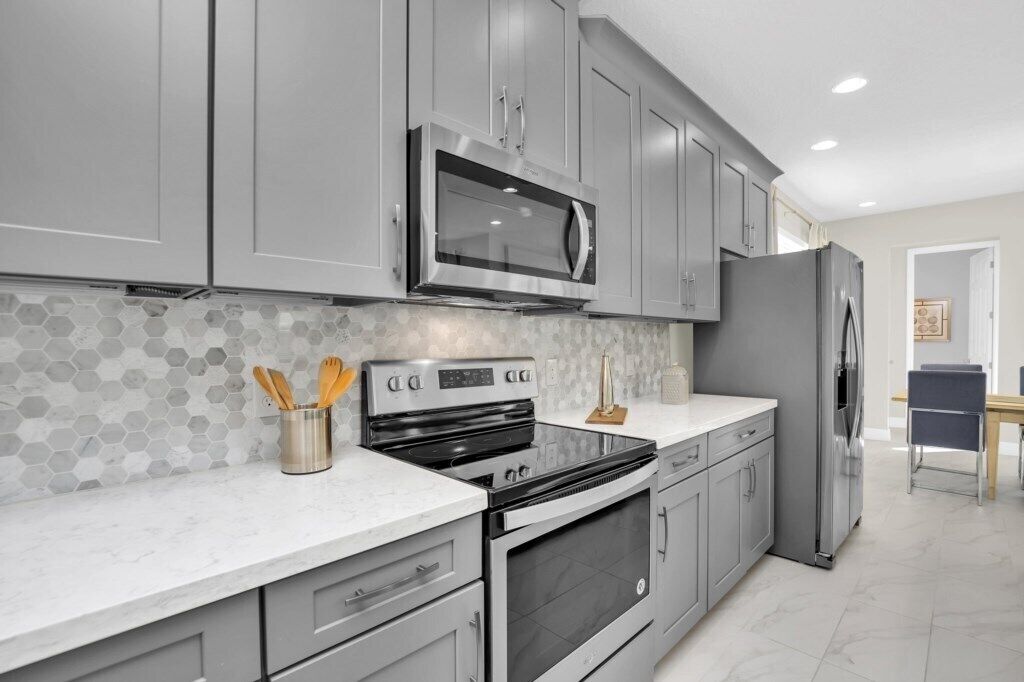 A modern kitchen with grey cabinets, stainless steel appliances, and a hexagonal tile backsplash.