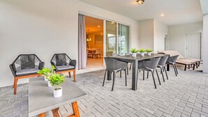 A patio with a table and chairs, a potted plant, and a sliding glass door leading to an indoor area.