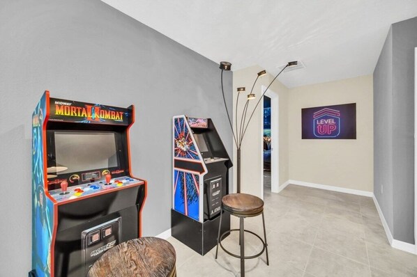 Une salle avec des jeux d’arcade, un tabouret et un panneau lumineux au néon.