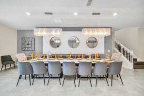 Une salle à manger moderne avec une longue table, des chaises grises et des luminaires suspendus.
