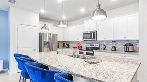 A modern kitchen with white cabinets, a granite countertop, and blue bar stools. - Ultimate 5 Bedroom Windsor Island Resort Pool  home (Davenport)