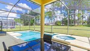 Un espace extérieur abrité avec une piscine, doté d’un plancher et d’une table en verre, entouré d’une clôture jaune et d’arbres.