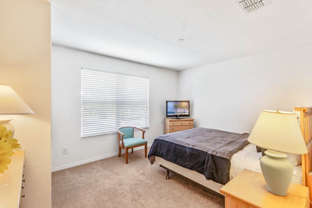 A bedroom with a bed, a chair, a TV, and a lamp.