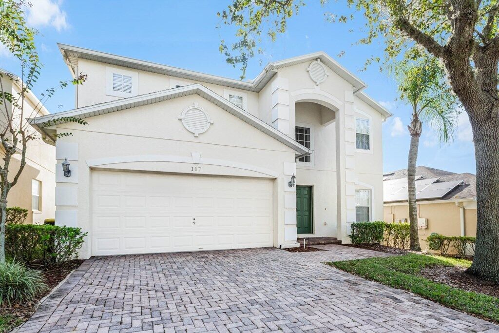 A two-story house with a white garage door, a green door, and a brick driveway.