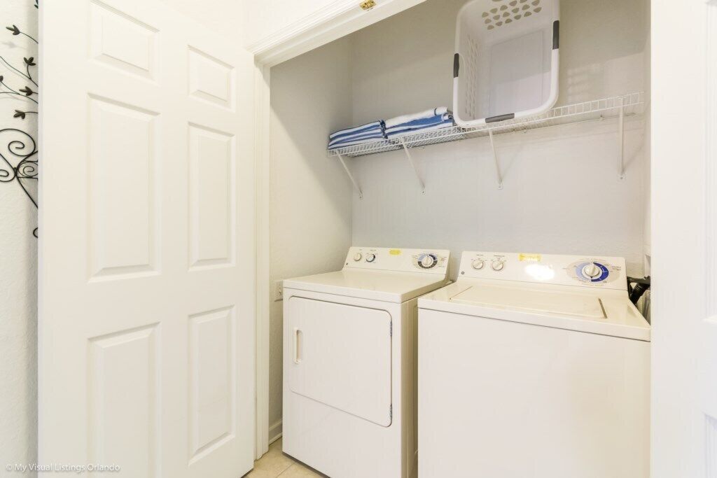 A laundry room with two white washing machines and a shelf above them.