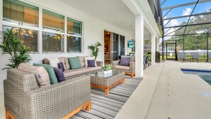 A covered outdoor seating area with wicker furniture and a pool.