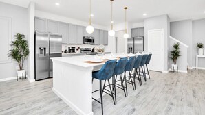 A modern kitchen with white cabinetry, stainless steel appliances, and a central island with bar stools.