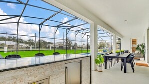 A covered outdoor area with a glass enclosure, a kitchen counter, and a dining table with chairs.