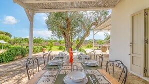 An outdoor dining area with a table set for four, surrounded by chairs, under a pergola.