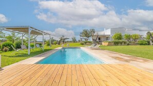 A swimming pool with a wooden deck, lounge chairs, and a white pergola.