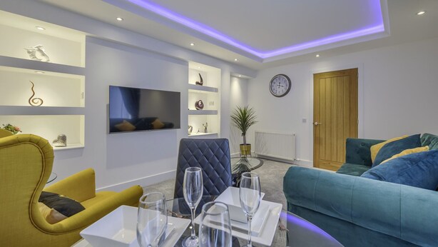 A modern living room with a sofa, armchair, and a dining table set with glasses.