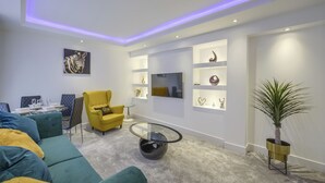 A modern living room with a sofa, armchair, coffee table, and a TV mounted on the wall.