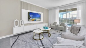 Une chambre d’hôtel moderne dotée d’une grande fenêtre, d’un téléviseur à écran plat fixé au mur, d’un canapé blanc, de deux petites tables rondes et d’un sol à motifs de marbre.