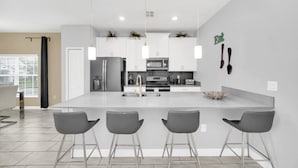 Una cocina moderna con armarios blancos, electrodomésticos de acero inoxidable y una isla central con taburetes de bar.