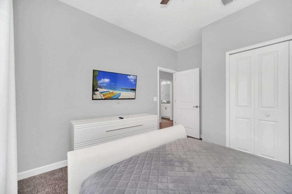 Ein Schlafzimmer mit Bett, einer weißen Kommode, einem an der Wand befestigten Fernseher und einem Schrank.