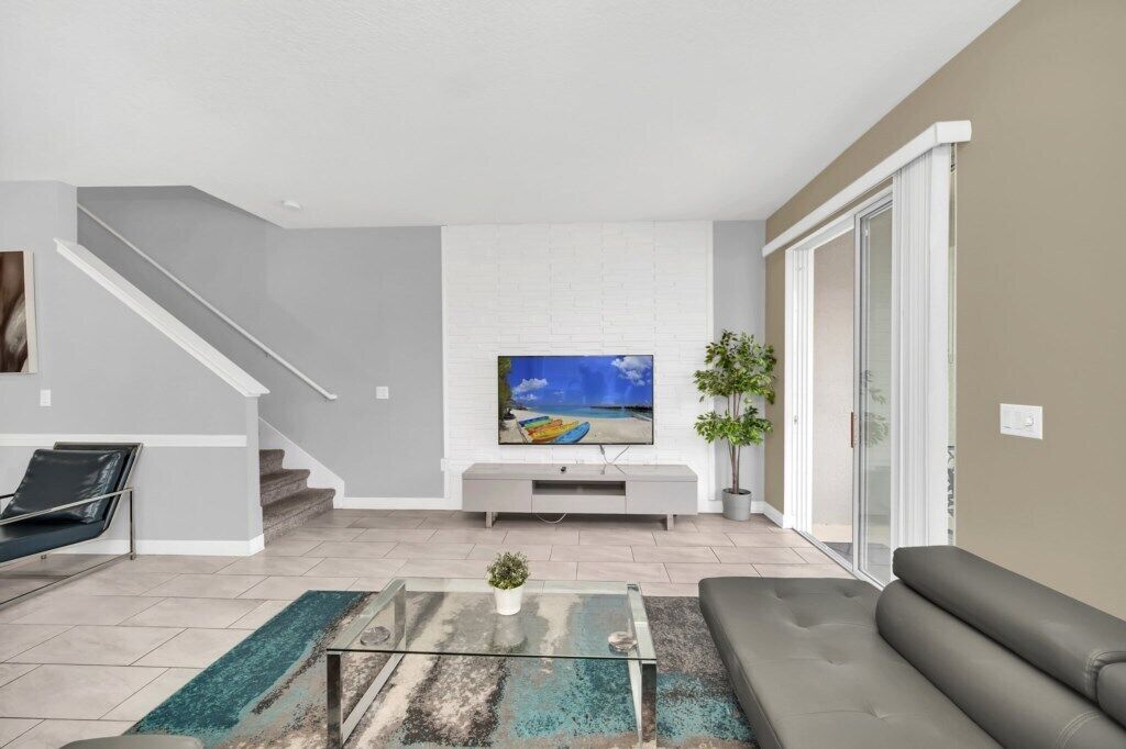 A modern living room with a flat-screen TV, a sofa, a coffee table, and a staircase.