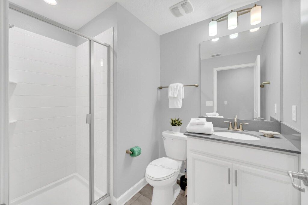 A modern bathroom with a glass shower enclosure, a toilet, a sink with a mirror, and a small potted plant.
