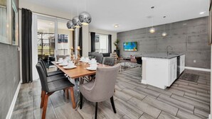 Una cocina moderna con una isla central, una zona de comedor con mesa y sillas de madera, y una sala de estar con televisor de pantalla plana.