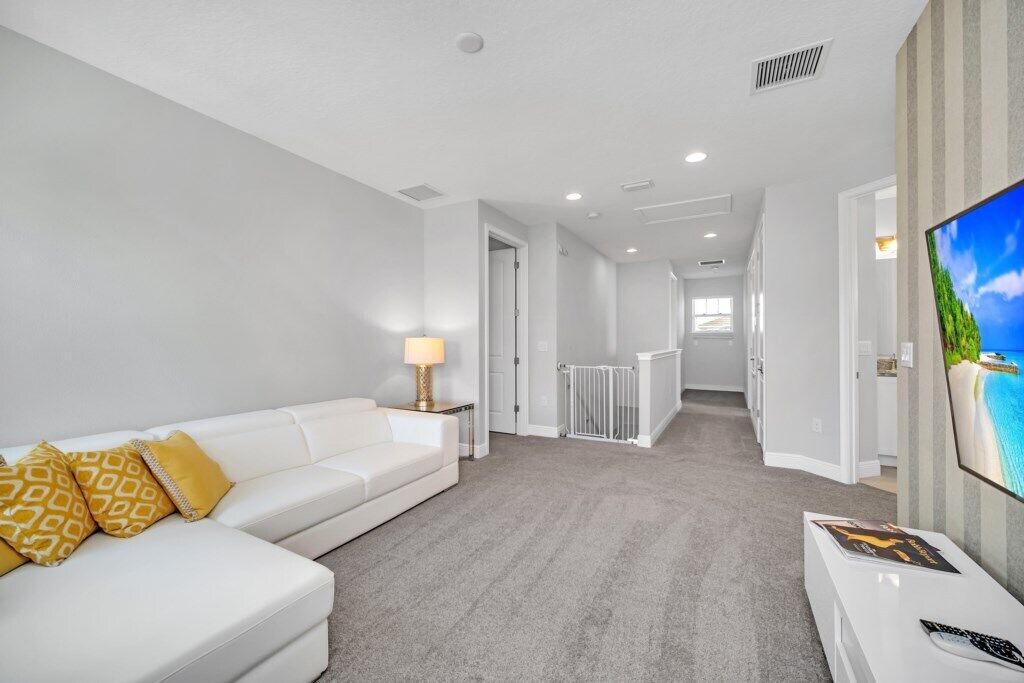 Une chambre d’hôtel moderne avec un canapé blanc, un téléviseur à écran plat et un sol recouvert de moquette.