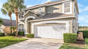 Une maison à deux étages avec un garage, une pelouse bien entretenue et un palmier.