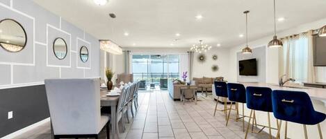 A modern kitchen with a dining area, featuring a long table, chairs, and a TV.