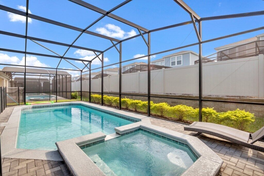 Un espace piscine doté d’une structure en verre, de deux bains à remous et d’une terrasse en briques.