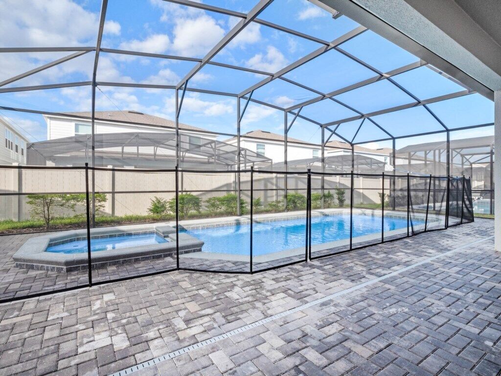 A covered swimming pool with a clear roof structure, surrounded by a brick patio.